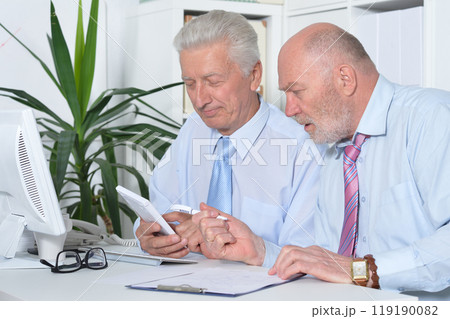 Two old business men sitting at desk and working Two old business men sitting at desk and working 119190082