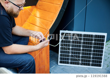 Cropped view of man connecting smartphone to photovoltaic solar panel. Integration of sustainable renewable energy into everyday life, demonstrating practical use of solar power for charging devices. Cropped view of man connecting smartphone to photovoltaic solar panel. Integration of sustainable renewable energy into everyday life, demonstrating practical use of solar power for charging devices. 119191388