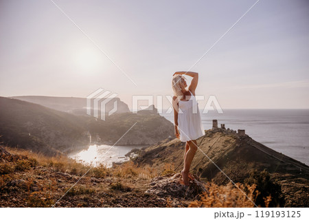 A blonde woman stands on a hill overlooking the ocean. She is wearing a white dress and she is enjoying the view. A blonde woman stands on a hill overlooking the ocean. She is wearing a white dress and she is enjoying the view. 119193125