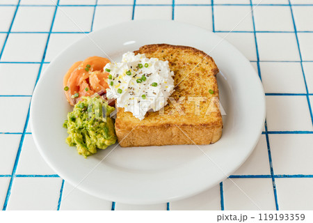 A beautifully colorful breakfast plate featuring crispy toast, ripe avocado, smoked salmon, and a rich, creamy topping 119193359
