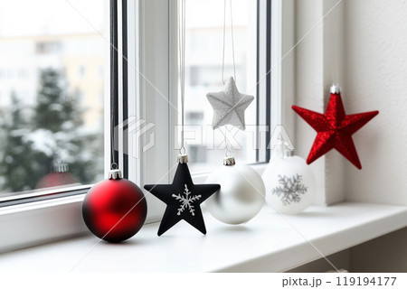 Red Christmas ornaments hanging on green branches beside a window with a snowy view outside. Concept of holiday decor Red Christmas ornaments hanging on green branches beside a window with a snowy view outside. Concept of holiday decor 119194177