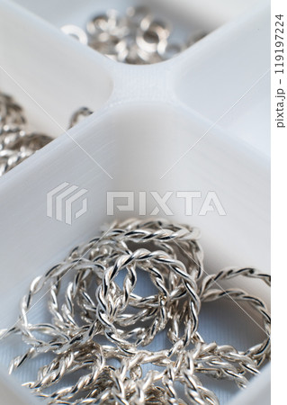 Close-up macro shot of small silver jewelry pieces lying in a white mesh box. DIY jewelry Close-up macro shot of small silver jewelry pieces lying in a white mesh box. DIY jewelry 119197224