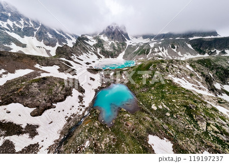 Aerial view of several high mountain lakes partially covered with snow and ice surrounded by high rocky mountain peaks Aerial view of several high mountain lakes partially covered with snow and ice surrounded by high rocky mountain peaks 119197237