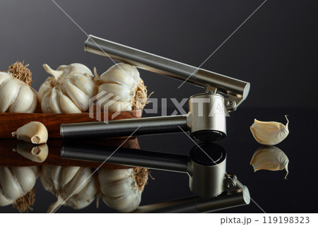 Garlic bulbs and garlic press on a black background. 119198323