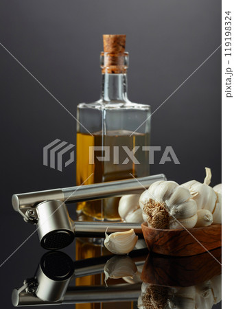 Garlic bulbs, garlic press, and bottle of vegetable oil. 119198324