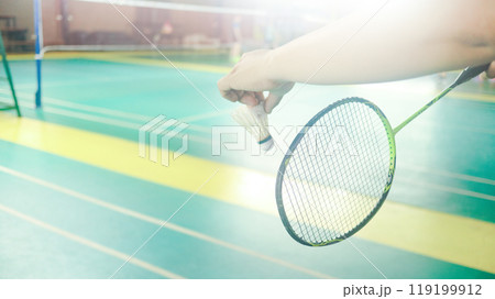 The badminton player holding a white shuttlecock and racket and standing at the net ready to serve. The badminton player holding a white shuttlecock and racket and standing at the net ready to serve. 119199912