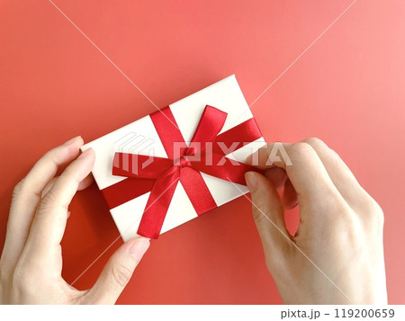 ギフトボックスの赤いリボンをほどく女性の手元 119200659