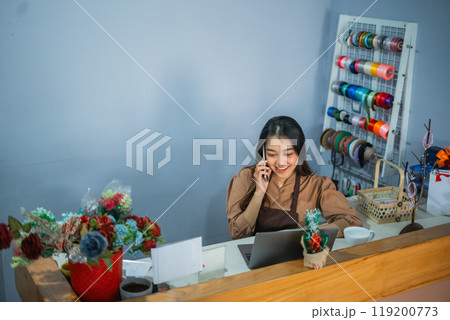 Asian girl employee making a phone call while working behind the counter 119200773