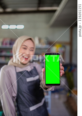 Happy Woman Holding Smartphone with Green Screen in a Creative Workspace 119201151
