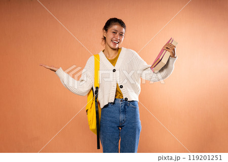 Cheerful Young Woman with a Colorful Backpack Posing Against an Orange Background Cheerful Young Woman with a Colorful Backpack Posing Against an Orange Background 119201251