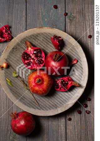 Pomegranates whole and open in a ceramic gray plate on a gray wooden background Pomegranates whole and open in a ceramic gray plate on a gray wooden background 119201337