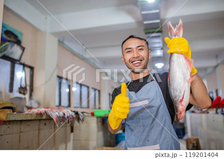 Cheerful fishmonger joyfully holding a fresh catch at the bustling seafood market Cheerful fishmonger joyfully holding a fresh catch at the bustling seafood market 119201404