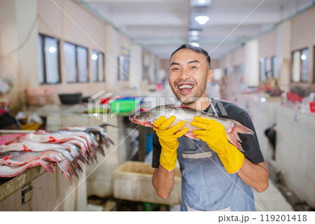 A Joyful Fisherman Holding His Fresh Catch in a Vibrant Seafood Market Today 119201418