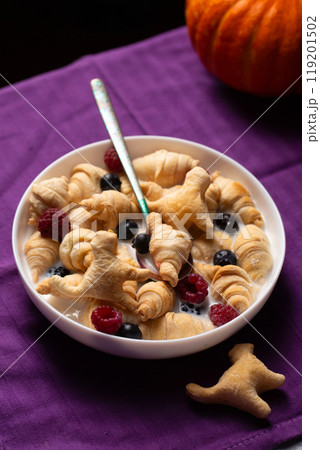 A quick breakfast of small croissants and cookies in the shape of a cat with berries and milk. Halloween breakfast concept 119201502