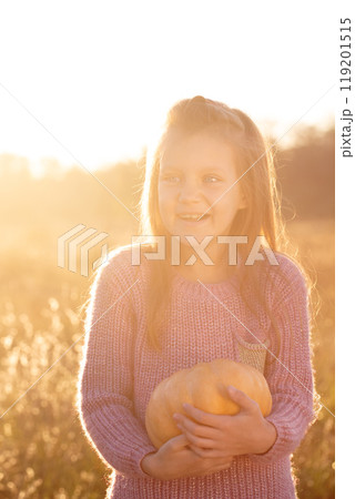 A young girl is holding a pumpkin in a field 119201515