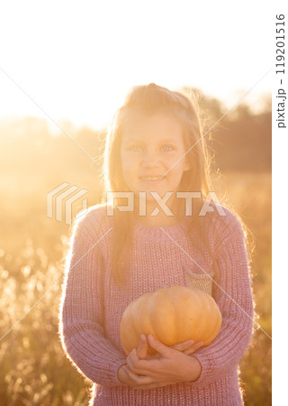A funny girl is holding a pumpkin in a field, backlight 119201516