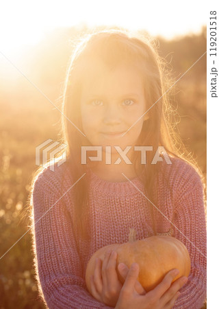 A lovely girl is holding a pumpkin in a field, backlight 119201518