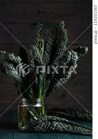 A bunch of kale, green leafy vegetables in a glass jar on a wooden table. Photo in a low key in a rustic style A bunch of kale, green leafy vegetables in a glass jar on a wooden table. Photo in a low key in a rustic style 119201567