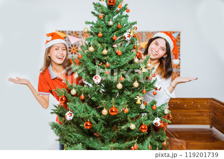 Joyful Friends Celebrating Christmas with a Beautiful Tree and Festive Hats 119201739