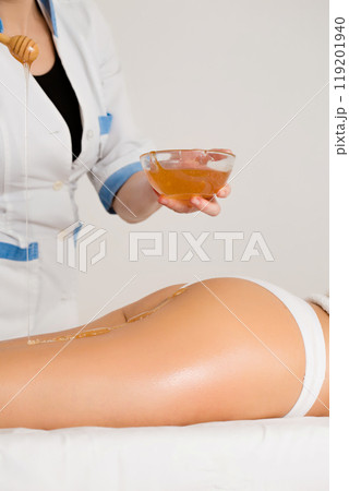 The masseuse applies honey to the patient's legs for an anti-cellulite massage 119201940
