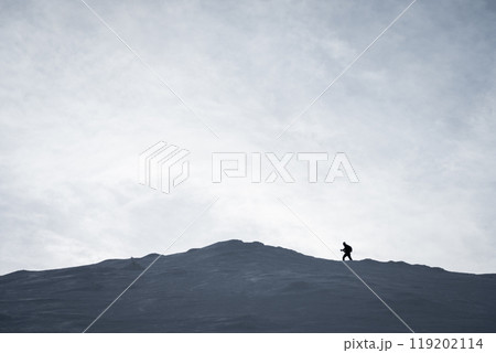 Silhouette shot of hiker approaching snowy mountain summit during winter 119202114