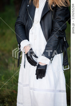 A woman in a vintage feminine white dress, black brutal jacket and black gloves, outdoors A woman in a vintage feminine white dress, black brutal jacket and black gloves, outdoors 119202294