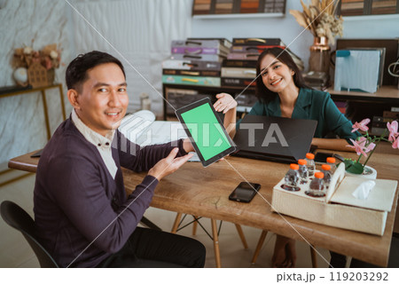 asian female shopkeeper smiling while pointing on the green screen digital tablet 119203292
