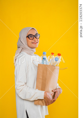 asian muslim woman posing sideways holding paper bag filled with plastic bottle asian muslim woman posing sideways holding paper bag filled with plastic bottle 119203374