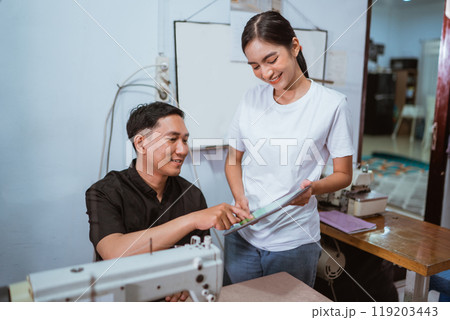 asian female employee showing the digital tablet to the male tailor asian female employee showing the digital tablet to the male tailor 119203443