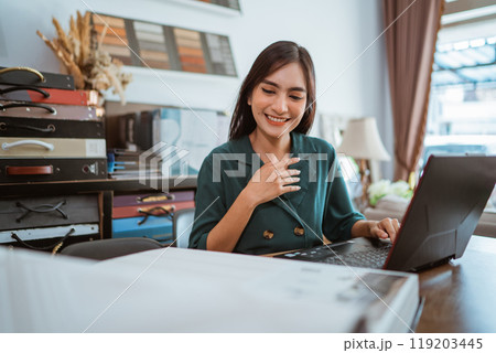 beautiful asian shopkeeper smiling while looking at window treatments catalogue book 119203445