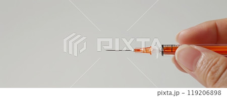 Hand holding a syringe filled with orange liquid against a white background. Medical equipment Banner with copy space 119206898
