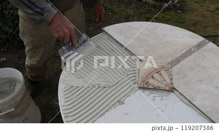 smoothing the solution applied for tiling the table surface with a shaped spatula, top view, decorating the table top with ceramic tiles fixed with mastic 119207386