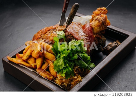 Roasted pork knuckle with potatoes and fresh herbs on wooden tray, stock food photography 119208922