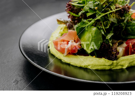Fresh salad with avocado cream and prosciutto, served on a black plate, perfect for gourmet dining Fresh salad with avocado cream and prosciutto, served on a black plate, perfect for gourmet dining 119208923