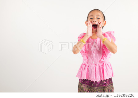 Portrait Thailand kid girl smiling traditional Thai dress costume use hand covering her mouth, studio shot isolated white background, kindergarten engaged in lively conversation, making announcement Portrait Thailand kid girl smiling traditional Thai dress costume use hand covering her mouth, studio shot isolated white background, kindergarten engaged in lively conversation, making announcement 119209226