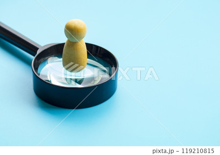 A wooden figure doll standing on top of magnifying glass with customizable space for text or ideas 119210815