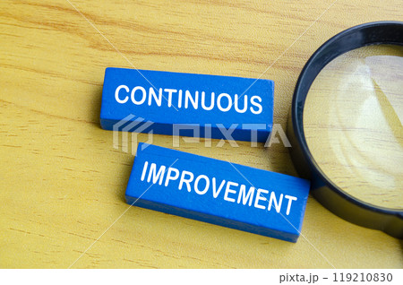 Continuous improvement text on blue wooden blocks with magnifying glass background. Continuous improvement concept Continuous improvement text on blue wooden blocks with magnifying glass background. Continuous improvement concept 119210830
