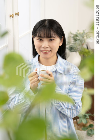 窓際でコーヒーカップを持って立つ女性 119212069