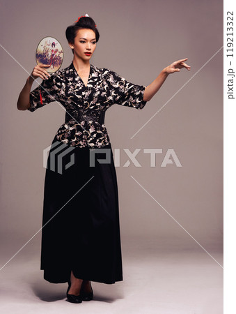 Fashion, dance and Japanese woman with geisha fan and Asian clothing with traditional outfit in studio. Culture, creative and heritage clothes with female person from Japan with brown background 119213322