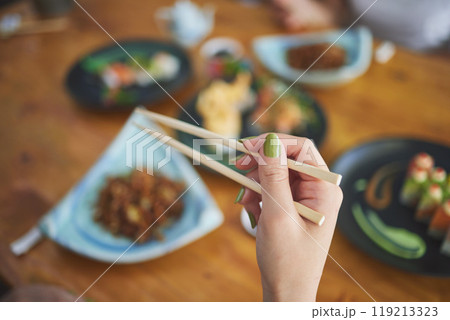 Chopsticks, hand and a person eating food at a restaurant for nutrition. Closeup of a hungry woman with wooden sticks or utensil for dining, Japanese culture and cuisine on diet with sushi on menu 119213323
