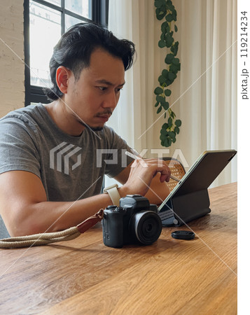 Serious photographer man working with his computer tablet at the wooden desk. Serious photographer man working with his computer tablet at the wooden desk. 119214234