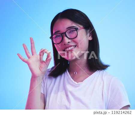 Woman, okay hands or sign for learning success, certified and excellence in tshirt and a blue, studio background. Happy young, asian person in glasses, portrait and yes or support emoji for education Woman, okay hands or sign for learning success, certified and excellence in tshirt and a blue, studio background. Happy young, asian person in glasses, portrait and yes or support emoji for education 119214262