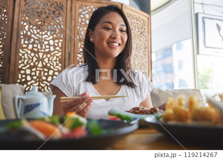 Asian, food and woman at a restaurant eating for dinner or lunch meal using chopsticks and feeling happy for nutrition. Plate, young and person enjoy Japanese cuisine, noodles or diet at a table 119214267