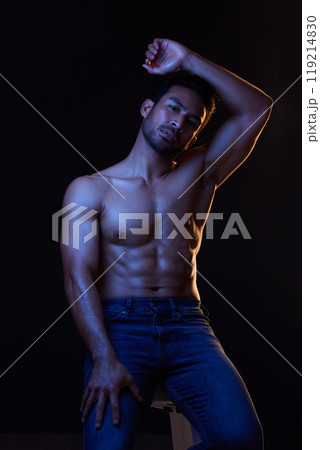 Bodybuilder man, abs and dark in studio portrait, jeans or muscle for healthy body by black background. Young guy, fitness and silhouette with face, stomach or strong for health, shirtless or fashion 119214830