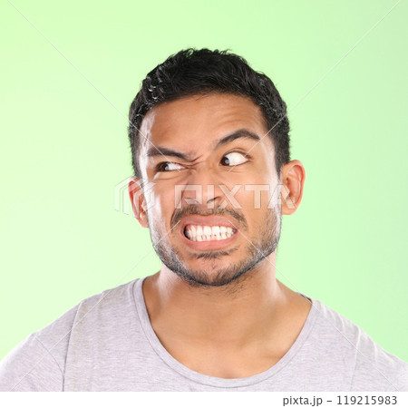 Man, angry face and disgust with awkward humor, comedy or nasty look on a green studio background. Frustrated male person or joker with goofy expression, attitude or upset behavior for wild anger Man, angry face and disgust with awkward humor, comedy or nasty look on a green studio background. Frustrated male person or joker with goofy expression, attitude or upset behavior for wild anger 119215983