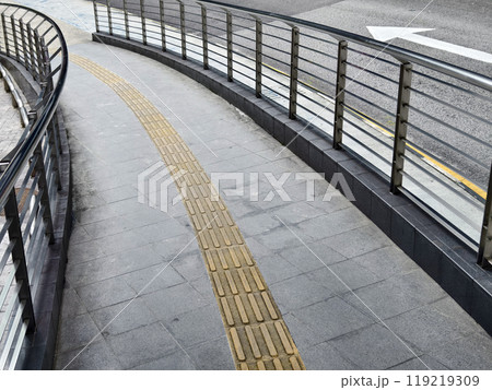 Curved path with guardrail and yellow line for blind people along the road 119219309