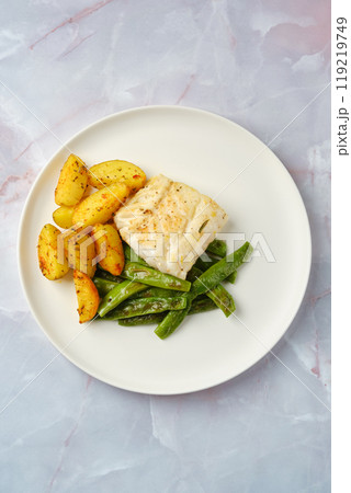 Delicious baked cod fillet served with seasoned potatoes and green beans on a white plate Delicious baked cod fillet served with seasoned potatoes and green beans on a white plate 119219749