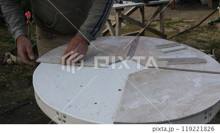laying out pieces of ceramic tiles on the surface of a round tabletop to form a pattern for decorating a table, a tiler works with the material in the process of creating exclusive furniture laying out pieces of ceramic tiles on the surface of a round tabletop to form a pattern for decorating a table, a tiler works with the material in the process of creating exclusive furniture 119221826