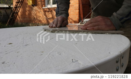 craftsman's hands press a thick piece of ceramic tile onto a layer of mastic on a table surface during the process of tiling, decorating outdoor homemade furniture with tile material 119221828