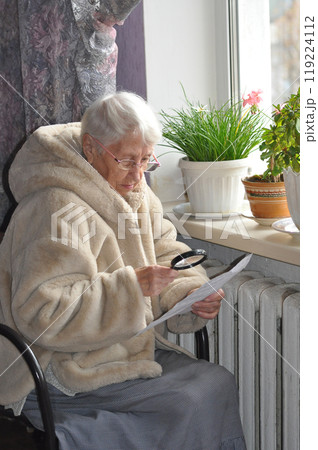 The senior woman holding gas bill in front of heating radiator. Payment for heating in winter. Freezing old people in Europe. The senior woman at home. 119224112